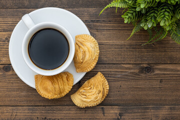 Top view of white coffee cup and curry puff pastry on wooden background