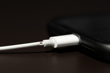 Close up view and low light. The PVC cable for charging the phone is damaged. Makes it possible to see the metal wires inside the electric current.