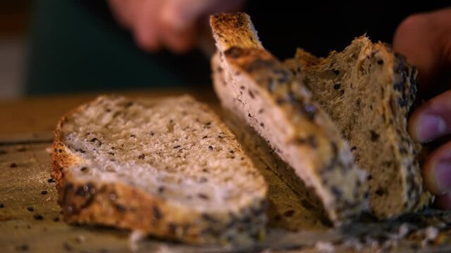 Homemade bread with sliced toasted sesame seeds, on a wooden board, in a warm setting, in slow motion. Finally, the slice is cut and falls slowly and smoothly onto the other.