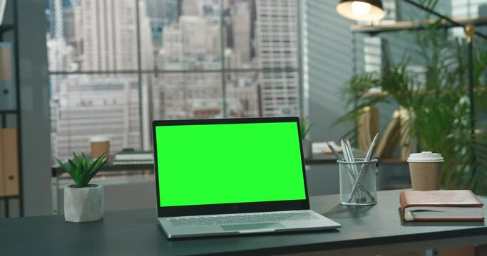 Personal computer with mock-up green screen monitor standing on the office desk with empty modern office in the background at the daytime. Business concept