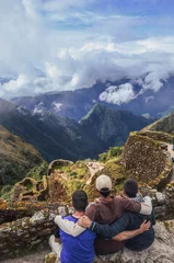 Photo sur Plexiglas Machu Picchu High angle view of three backpacker male friends hugging each other on Phuyupatamarca ruins with the huge valley in front of them. Inca trail to Machu Picchu in Peru. South America