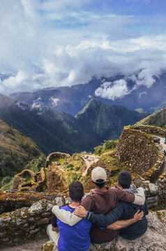 High angle view of three backpacker male friends hugging each other on Phuyupatamarca ruins with the huge valley in front of them. Inca trail to Machu Picchu in Peru. South America