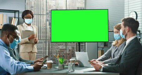 Serious involved business people wearing protective masks spending time together at the modern office, talking and using projector. Brunette multiracial woman looking at her colleagues and discussing - Powered by Adobe