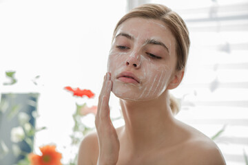 Beautiful young girl cleansing face with cosmetic facial skincar