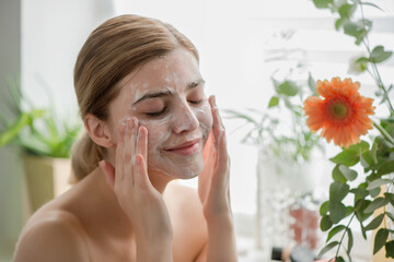 Beautiful young girl cleansing face with cosmetic facial skincar