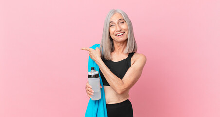 middle age white hair woman looking excited and surprised pointing to the side with a towel and...