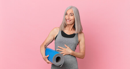 middle age white hair woman laughing out loud at some hilarious joke and holding a yoga mat. fitness concept