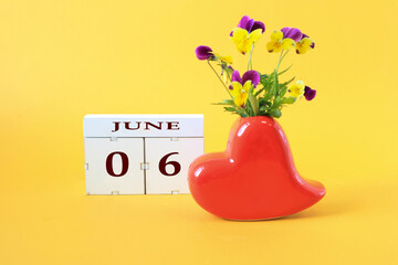 Calendar for June 6 : the name of the month of June in English, the numbers 0 and 6, a vase in the shape of a red heart with a bouquet of violets on a yellow background