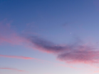 Beautiful sunset with pink clouds on clear blue sky with  sickle of the waxing moon. Colorful panorama of heavens. Peaceful atmosphere of evening. Dusk time of a day.
