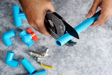 Cutting pvc water pipe with scissors on gray background.	