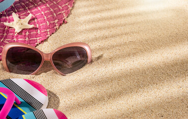 Large round summer pink hat, with sunglasses and flip flops and star fish on beach sand, top view, copy space