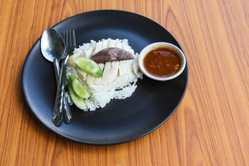 Chicken rice, top view with spoon and fork in the black dish isolated on wooden background closeup.