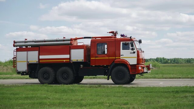 A fire truck is driving on the road towards the runway at the airport. Shooting from the side
