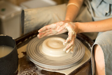 female hands make dishes from clay on a potter's wheel