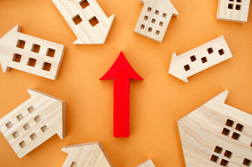 Miniature wooden houses and red arrow up. The concept of increasing the cost of housing. High...