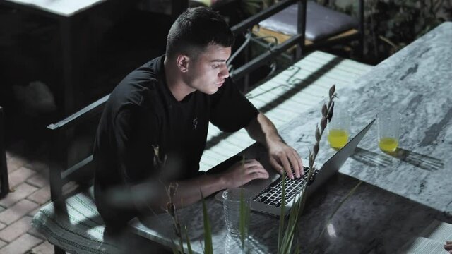 Closeup of developer man hands typing, coding on a laptop while on in a beach bar at night, business freelancer working on vacation
