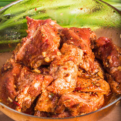 Marinated raw pork pieces with garlic and hot sauce in a glass bowl, close-up