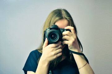 Girl with a SLR camera in her hands. Front view. The camera lens is directed towards the viewer....