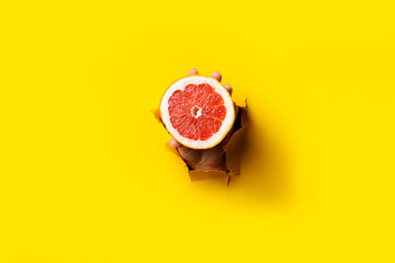 A woman's hand holds a cut grapefruit in a torn cardboard yellow background