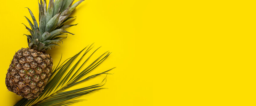 fresh ripe whole yellow pineapple and lsit palms on a yellow background. Top view, flat lay. Banner