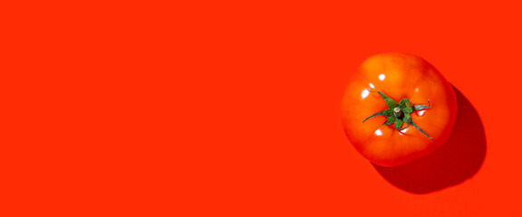 one ripe red tomato on a red background. Top view, flat lay. Banner