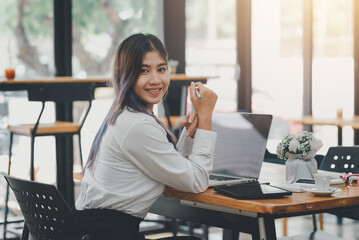 Obraz premium Asian businesswoman sitting at work on his laptop looking at the camera. at the office.