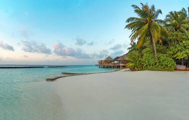 Obraz na płótnie Canvas Amazing wide panorama of tropical Maldives island. Exotic beach background with blue lagoon, turquoise water and palm trees during beautiful sunrise. 