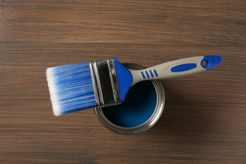 Can of blue paint and brush on wooden background, top view