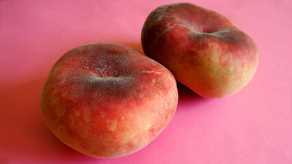 close up two pink whole fig peaches lie on a pink background. side view. artificially derived fruit rich in vitamins