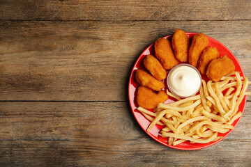 Tasty chicken nuggets and French fries served with mayonnaise on wooden table, top view. Space for text