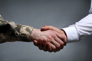 Soldier and businessman shaking hands against grey background, closeup - obrazy, fototapety, plakaty