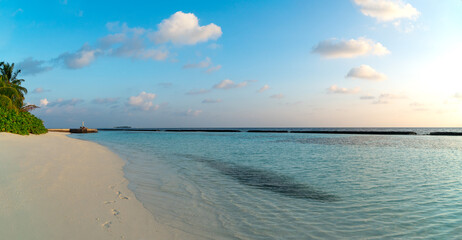 Amazing wide panorama of tropical Maldives island. Exotic beach background with blue lagoon, turquoise water and palm trees during beautiful sunrise. 