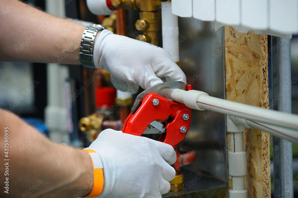 Wall mural Plumber hands in gloves cut plastic pipe with the pipe cutter