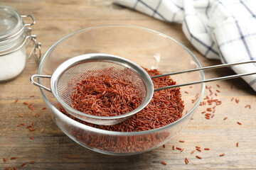 Sieve with brown rice in bowl on wooden table