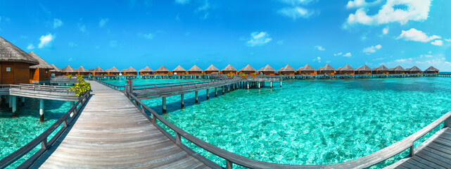 Fototapeta premium Amazing wide panorama of tropical Maldives island on a sunny day. Exotic vivid beach background with blue turquoise lagoon and palm trees. Luxurious holiday and romantic honeymoon destination.