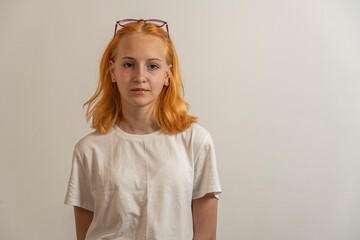 Portrait of a teenage girl with red hair and a white T-shirt on a light background