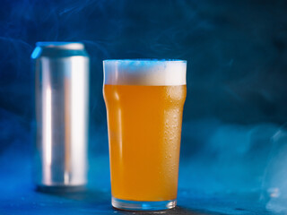 New England IPA beer glass and beer can on dark blue wooden background. Craft beer