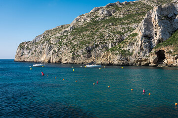 Two boats anchored on a beach with turquoise blue waters at the foot of a cliff in summer, Javea, Spain