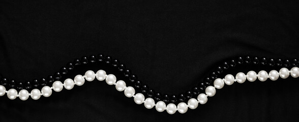Banner in a dark key with two strings of pearl beads in white and black colors on a gray fabric. An elegant banner with space for text about luxury and the pearl industry.