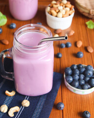 Blueberry smoothie on a wood platform with blueberries and nuts scattered around