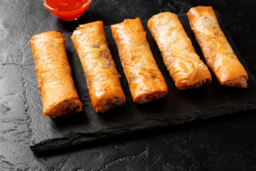 Fresh fried spring rolls stuffed with red cabbage and carrot served with sweet chili dip sauce.Black background.