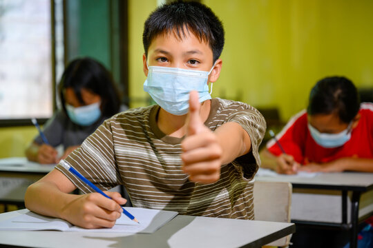 Asian Elementary School Boy Wearing A Mask To Prevent Coronavirus (COVID 19) Doing Education In A Classroom At A Rural School On The First Day Of Semester.