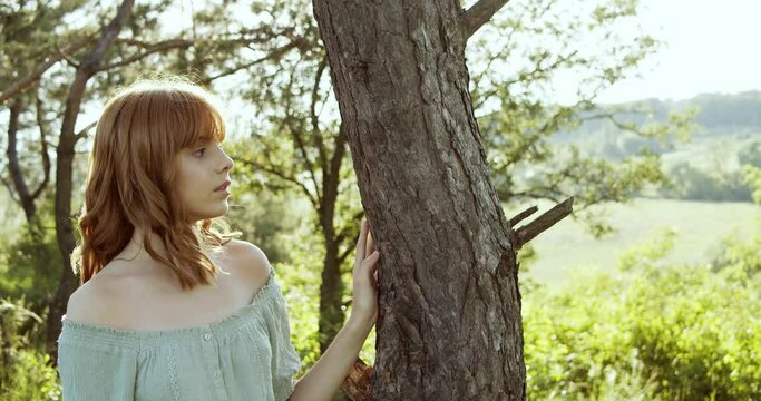 Attractive European chestnut teen girl with natural makeup has a pleasure of nature near a tree in forest on a sunny day