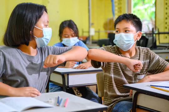 Asian Elementary School Students Wearing A Mask To Prevent Coronavirus (COVID 19) Doing Education In A Classroom At A Rural School And Greeting Each Other On The First Day Of The Semester.