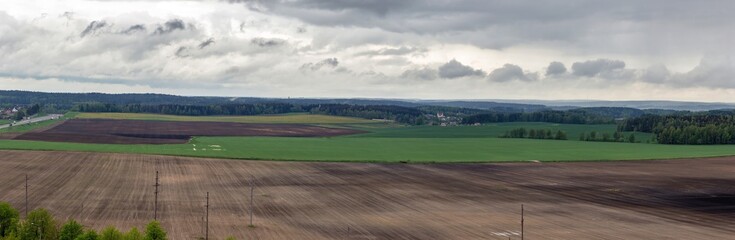 Panorama of freshly plowed agricultural fields under a cloudy sky. Detailed natural landscape with fields and forests of Belarus