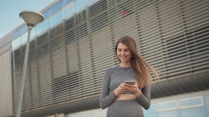 Fototapeta premium Portrait woman looking at smartphone while running outdoor. Close-up Of A Young Beautiful Sports Fitness Girl Holding A Smartphone In The Hands, Using A Fitness App. Modern City Shooting On the Street