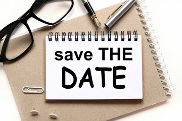 save the date.text on paper, on a notebook on a craft background, near glasses