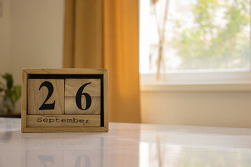 Wooden blocks of the calendar represents the date 26 and the month of September on the background of a window, curtain and a plant.