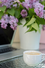 On the table are a bouquet of lilacs and a computer, a cup of coffee. Concept, work at home.