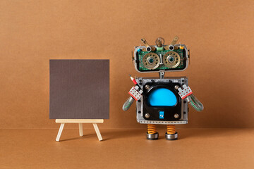 A robot artist poses with a pencil next to a wooden easel and a blank sheet of brown paper....